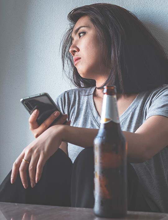 Женщина сидит с телефоном рядом с пивной бутылкой